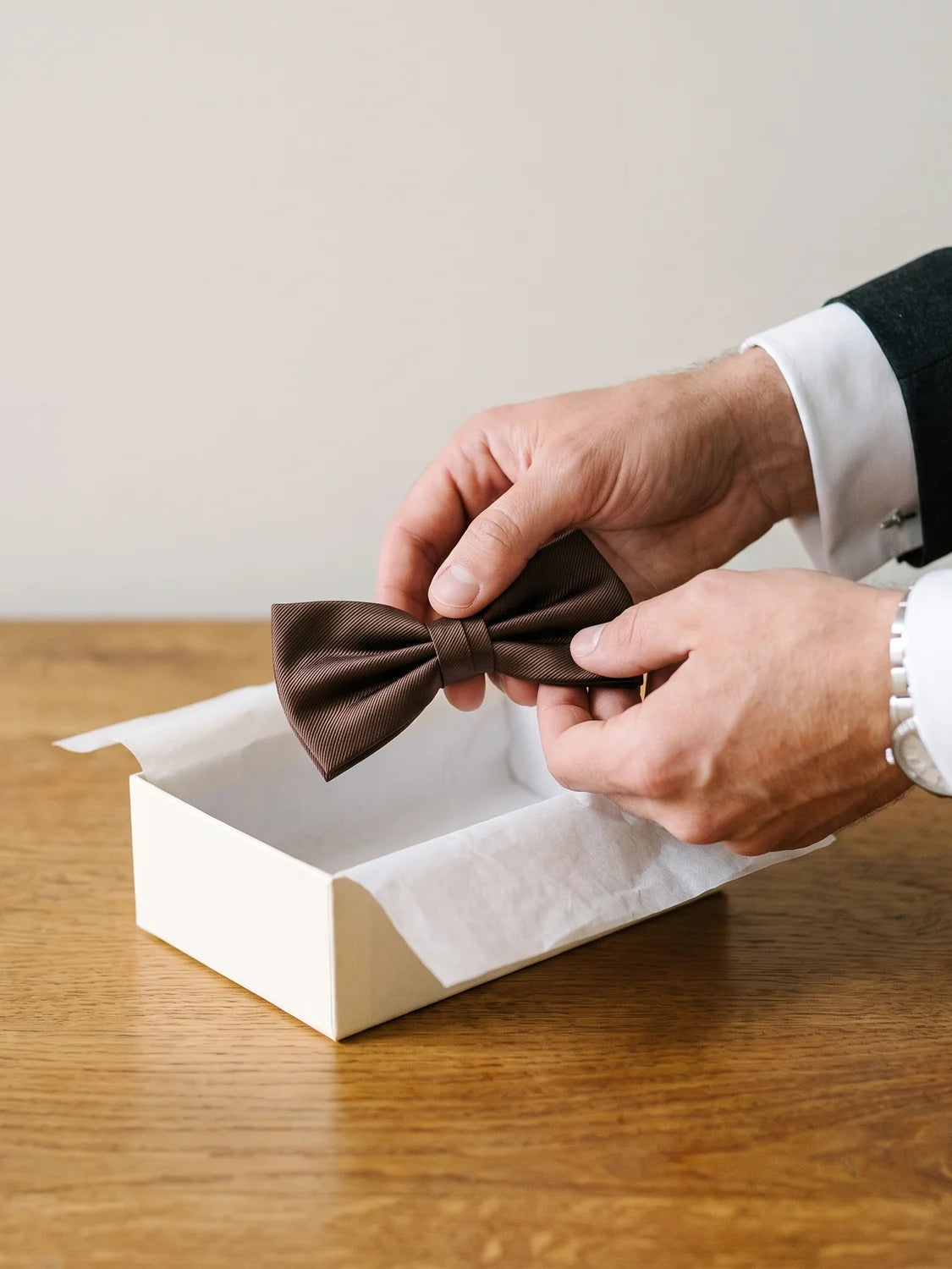 Hände nehmen eine braune Fliege aus einer cremefarbenen Geschenkbox
